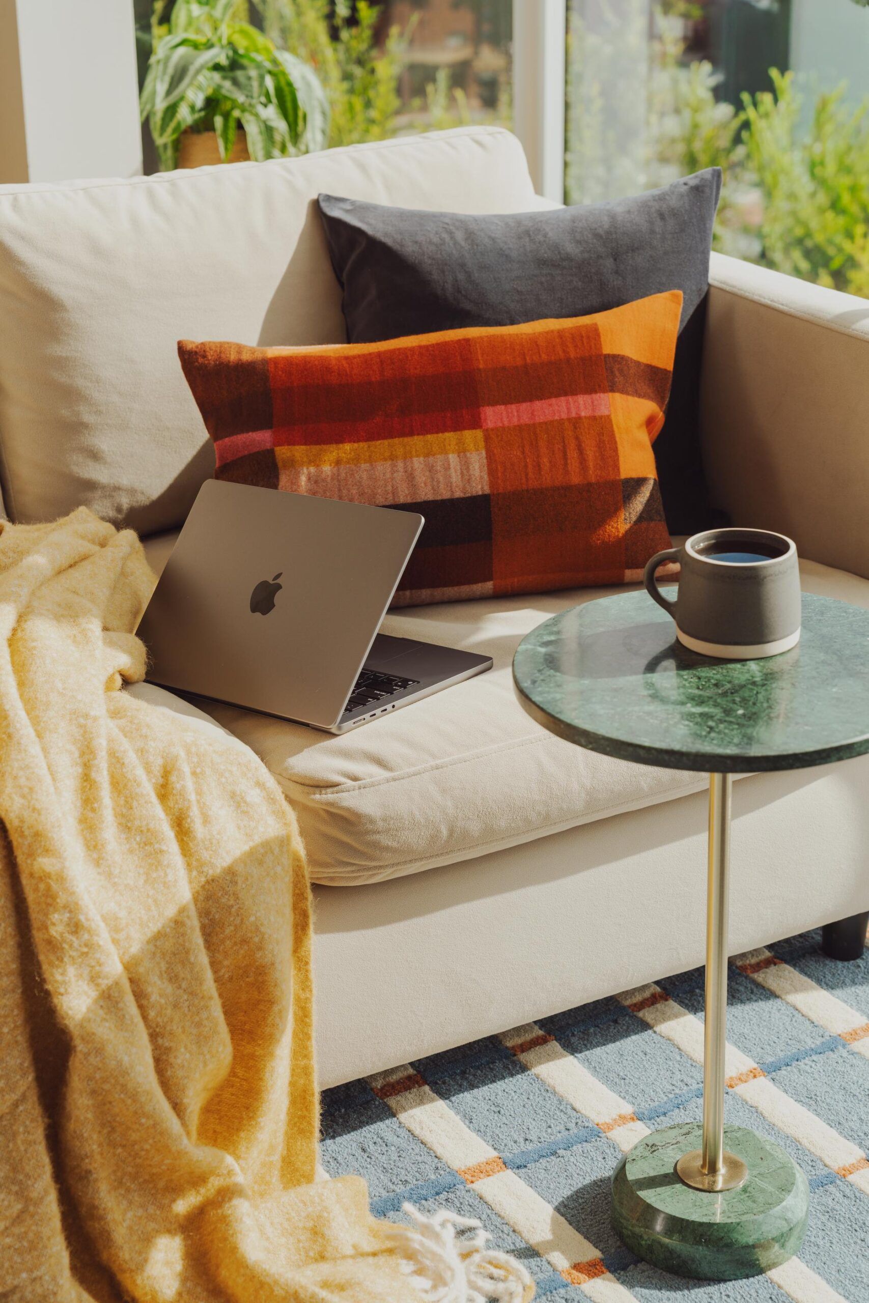 OSLO Coliving cozy sofa with a laptop, colorful pillows, a yellow blanket, and a coffee mug on a small round table.