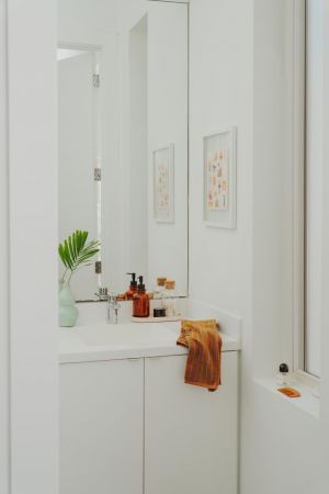 OSLO Coliving a modern white bathroom with a sink, soap dispensers, a green vase, and an orange towel on the counter.