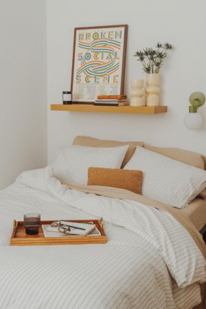 OSLO Coliving cozy bed with striped bedding, a wooden tray, and a shelf with decor and a colorful framed print above.