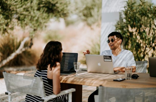 Two people sitting at an outdoor table in a garden with laptops